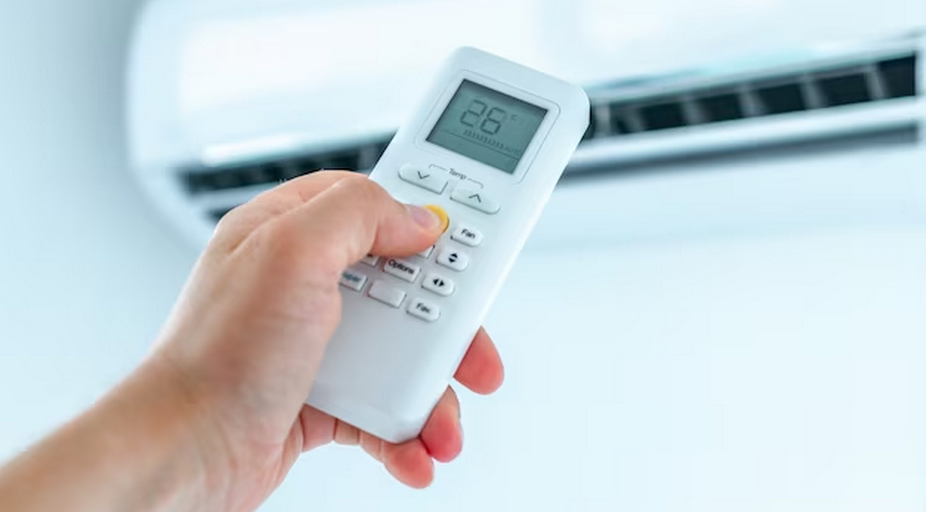 Hand with AC remote displaying temperature, blurry air conditioner in the background.
